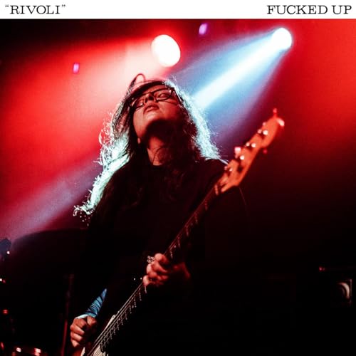 Musician playing bass guitar onstage, illuminated by red and white lights.