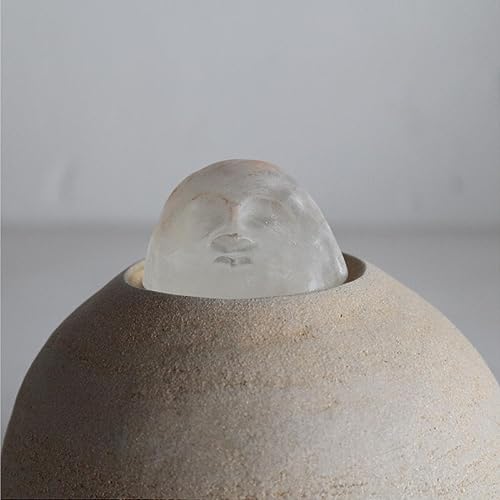 Close-up of a sculpted face emerging from a textured, rounded form.