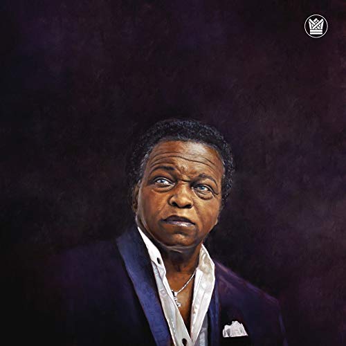 Portrait of Lee Fields in a suit, against a dark, textured background.