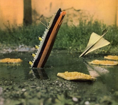 Miniature ship sinking in water with paper airplanes and debris.