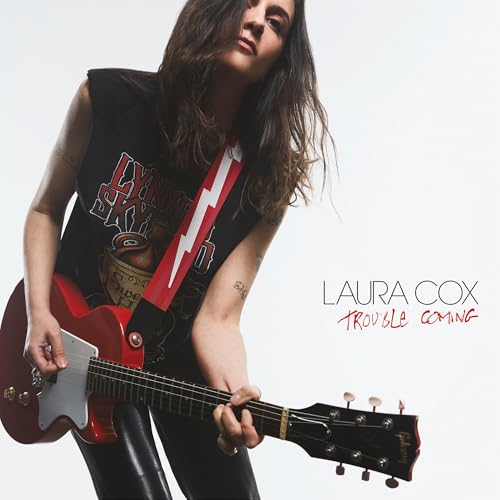 Laura Cox poses with a red electric guitar, album title visible.