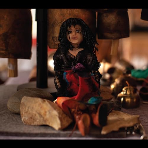 Doll with dark hair and floral adornment amidst scattered objects.