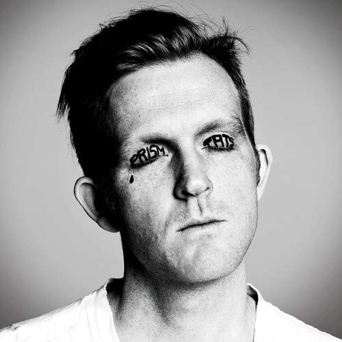 Black and white portrait of a man with "PRISM TATS" written on his face.