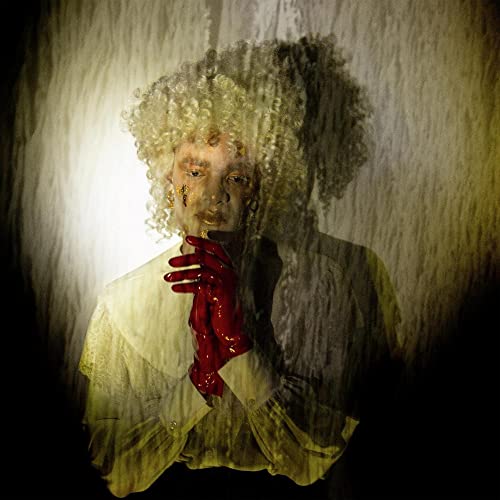 Person with pale skin, curly wig, and red gloves, distorted image.