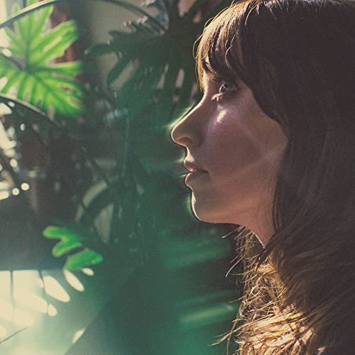 Profile of a woman with long dark hair, lush green foliage background.