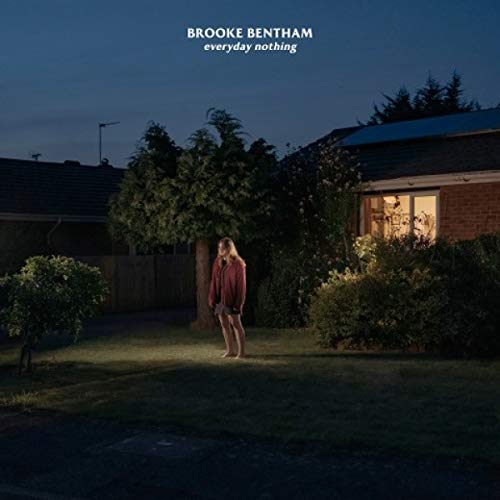 Woman stands barefoot in a yard at night with a house and trees behind her.