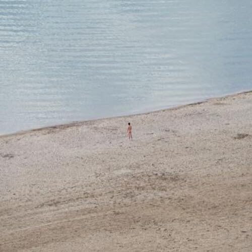 Aerial view of a lone person standing on a sandy beach.