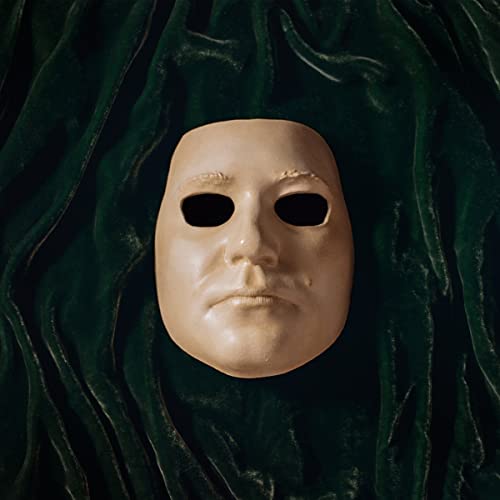 Pale face mask with dark eye holes against dark green velvet.
