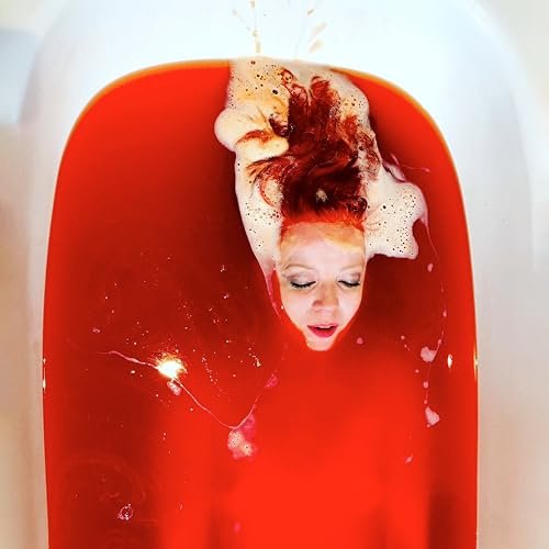 Woman with red hair submerged in red liquid with white foam.
