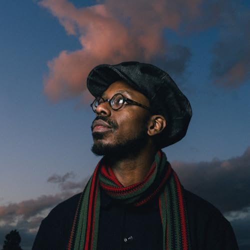 Shabaka Hutchings, a Black musician, wearing a cap and scarf, looks upward.