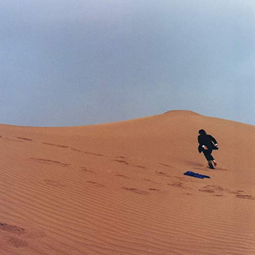 Person running across orange sand dunes under a pale blue sky.