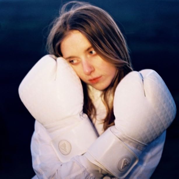 Woman with pale skin and brown hair wearing large white boxing gloves.