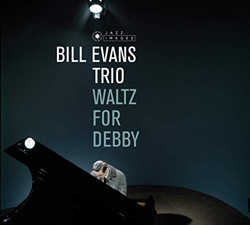 Man in suit sitting at piano with spotlight shining down, dark background.