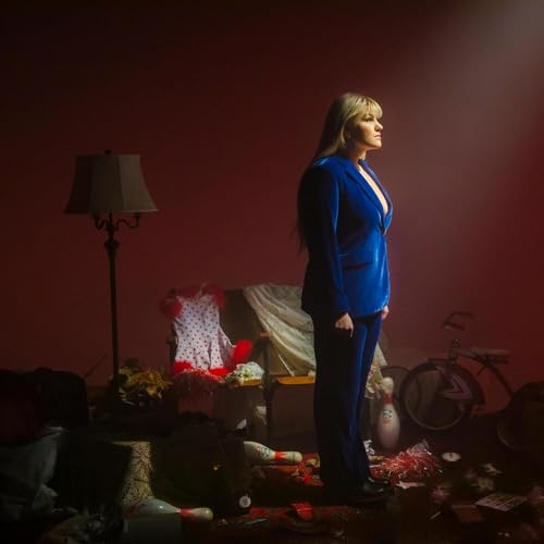 Maddie Zahm in a blue suit stands in a cluttered, dimly lit room.