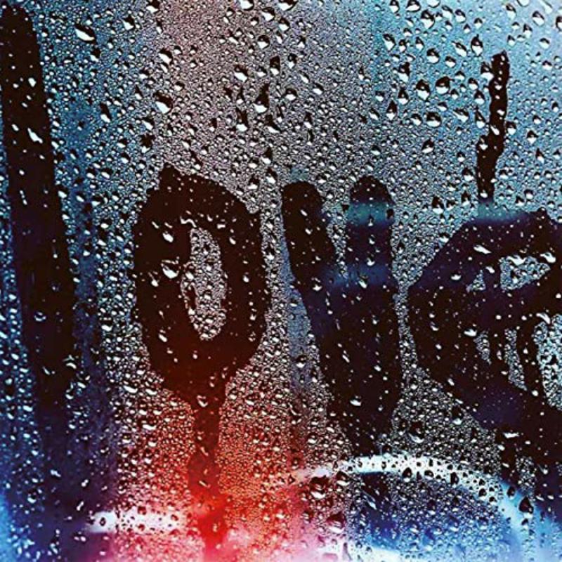 Rain-streaked window with blurred graffiti and red and blue lights.
