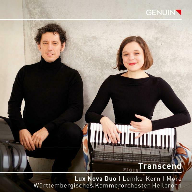 Man and woman in black clothing posing with an accordion againstC against a wall.