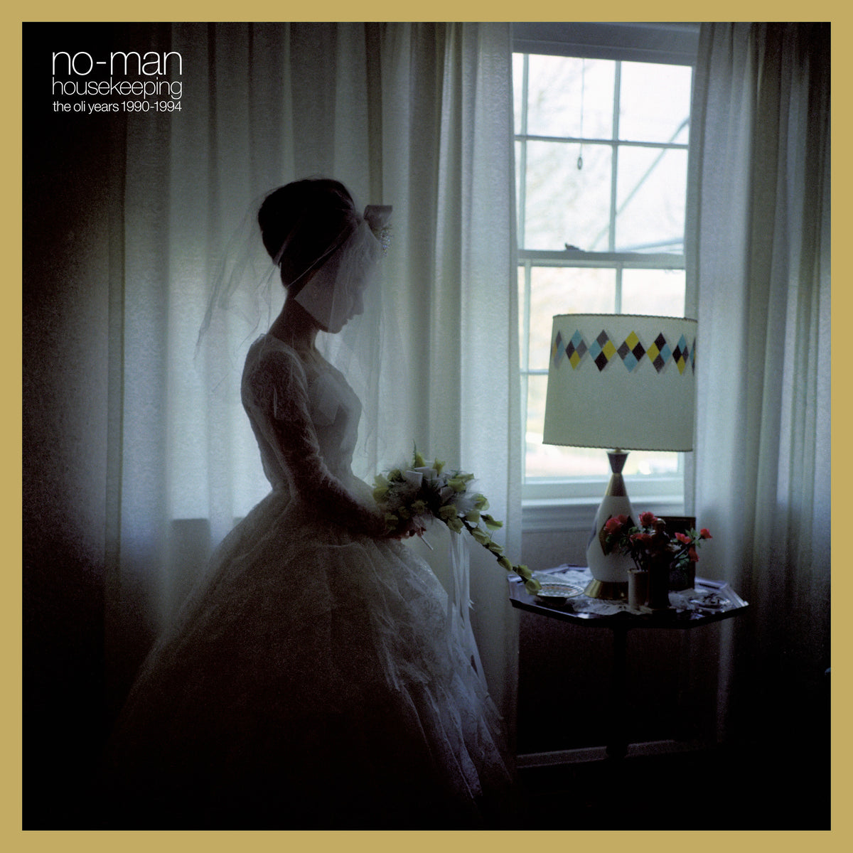 Bride in white dress standing near a window with a lamp.