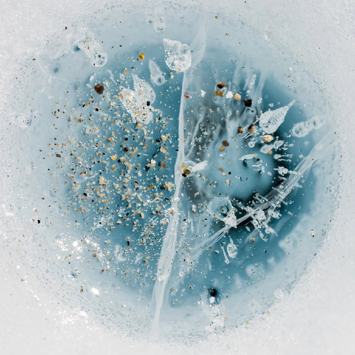 Abstract close-up of ice with debris, blue center, and white surroundings.