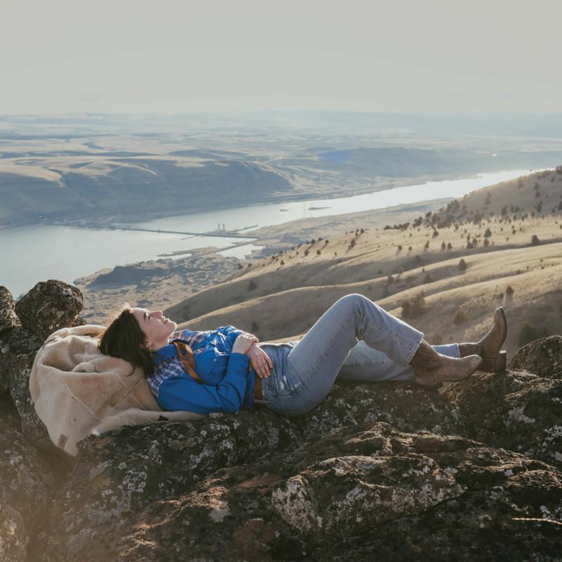 Woman in denim lying on rocks overlooking a river valley.