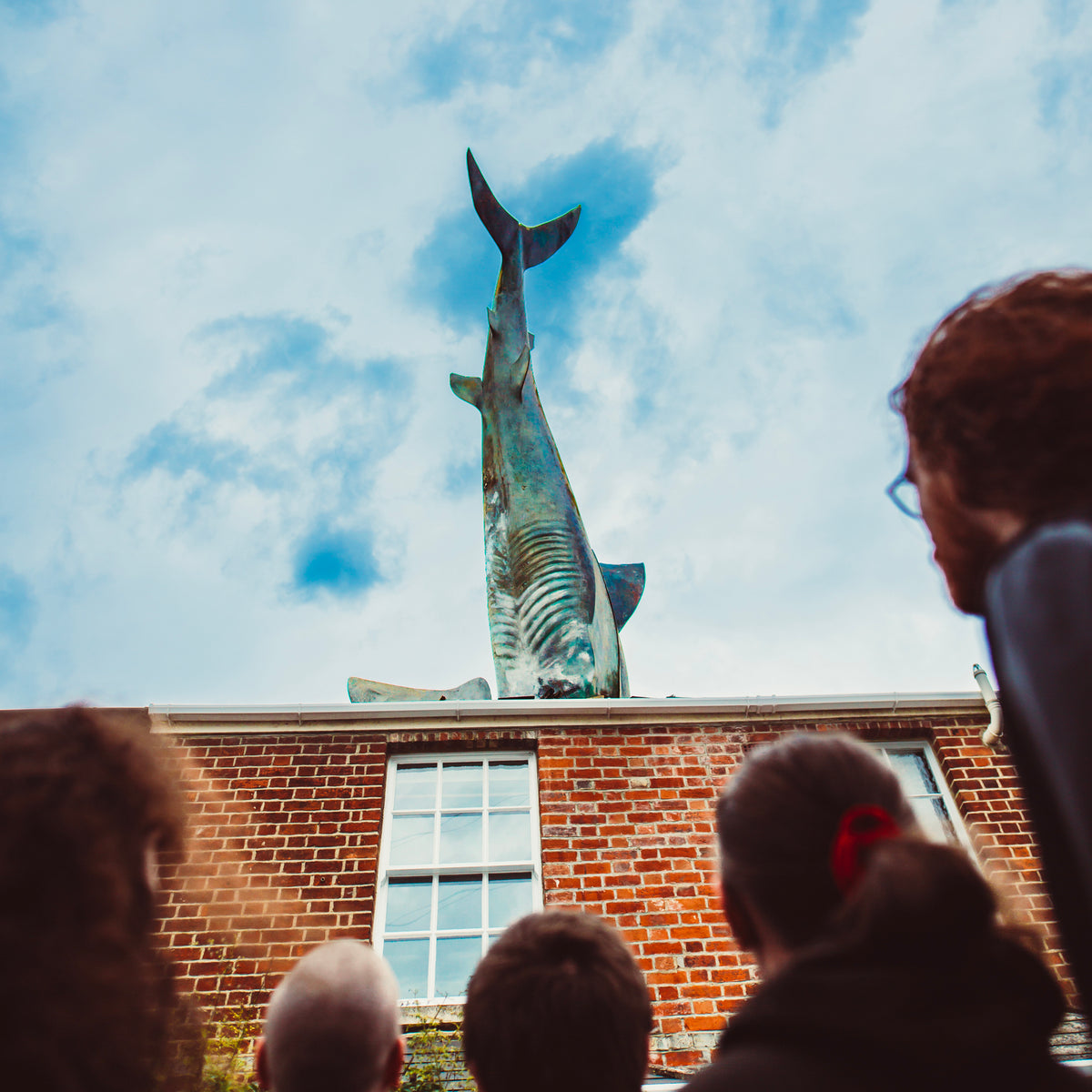 Sculpture of a breaching whale atop a brick building, viewed from below.