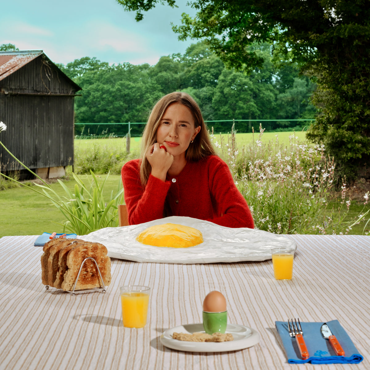 Woman in red poses with breakfast food in a rural setting.