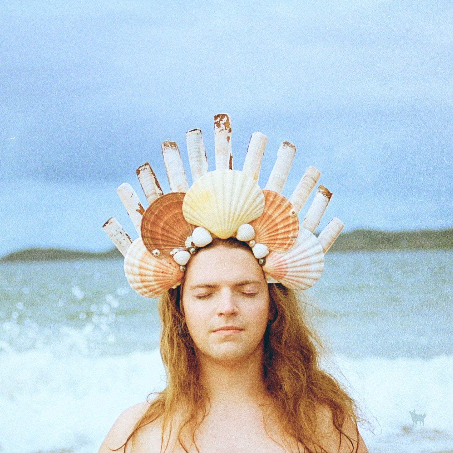 Person with seashell crown, eyes closed, ocean background.