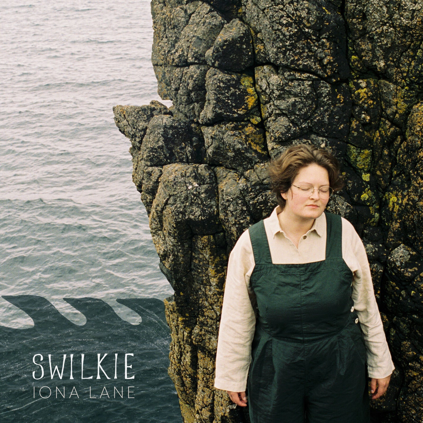 Album cover: woman with curly hair beside a rocky coastline.