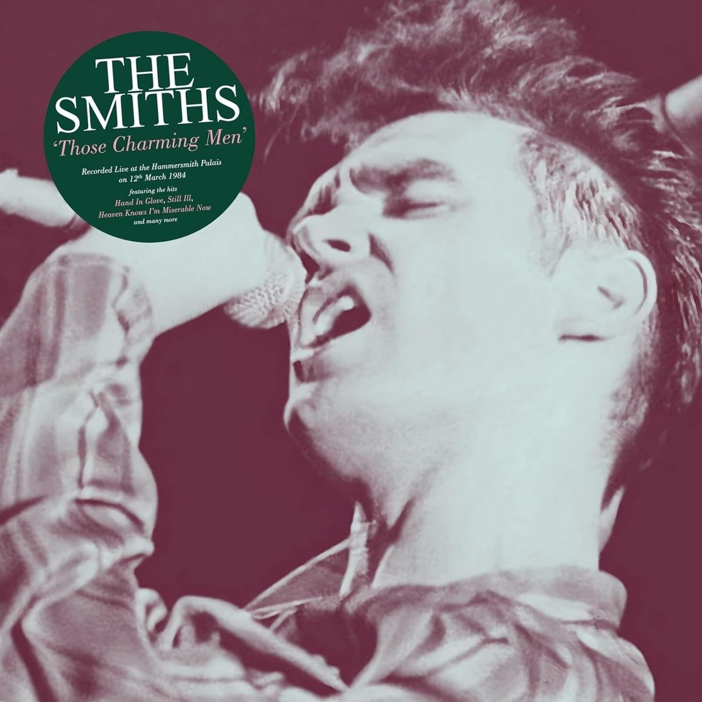 A monochrome close-up of a singer performing into a microphone with a green circular label.