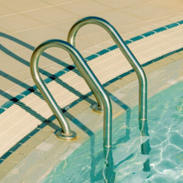 Metal pool ladder railings leading into clear blue water beside a tiled deck.