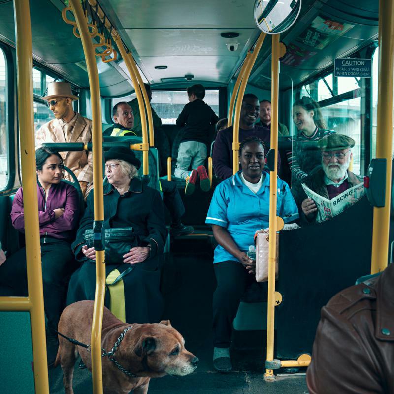 People and a dog sit on a public bus, looking in different directions.