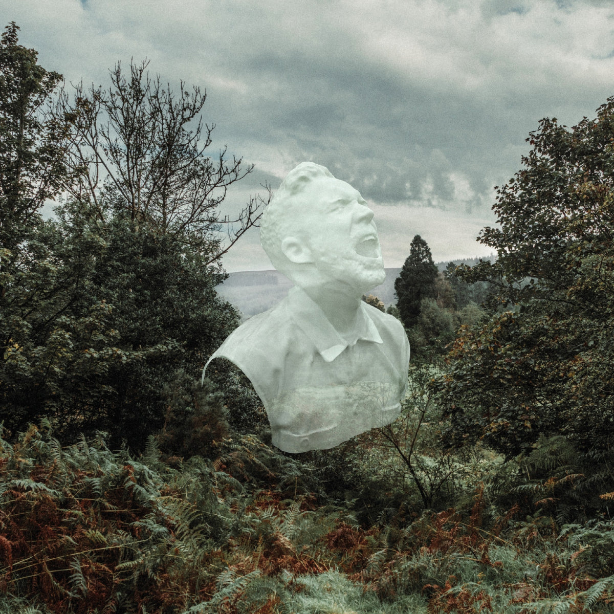 White bust of a man amidst lush green foliage under a cloudy sky.