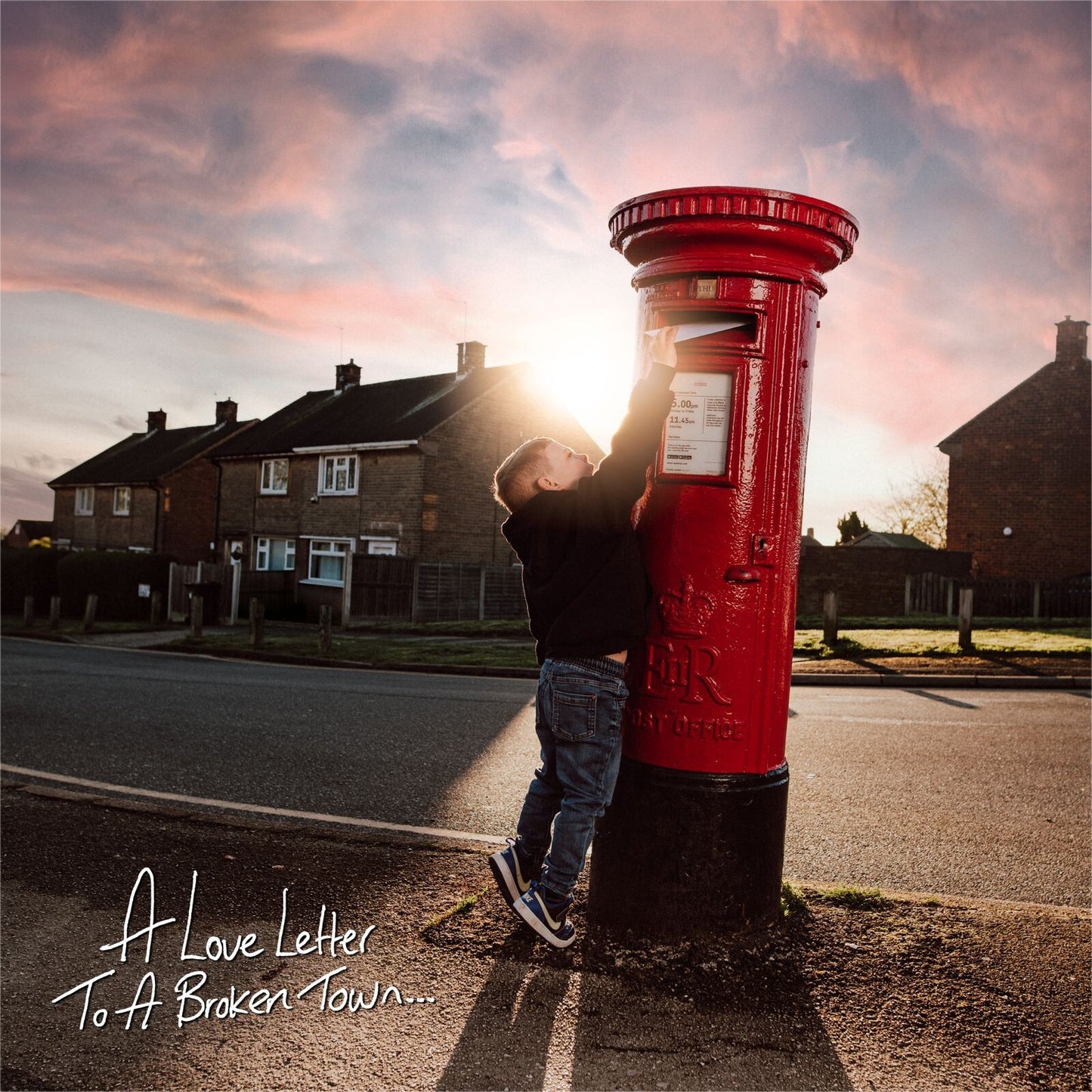 Boy leaning on a red postbox with houses and a sunset backdrop.