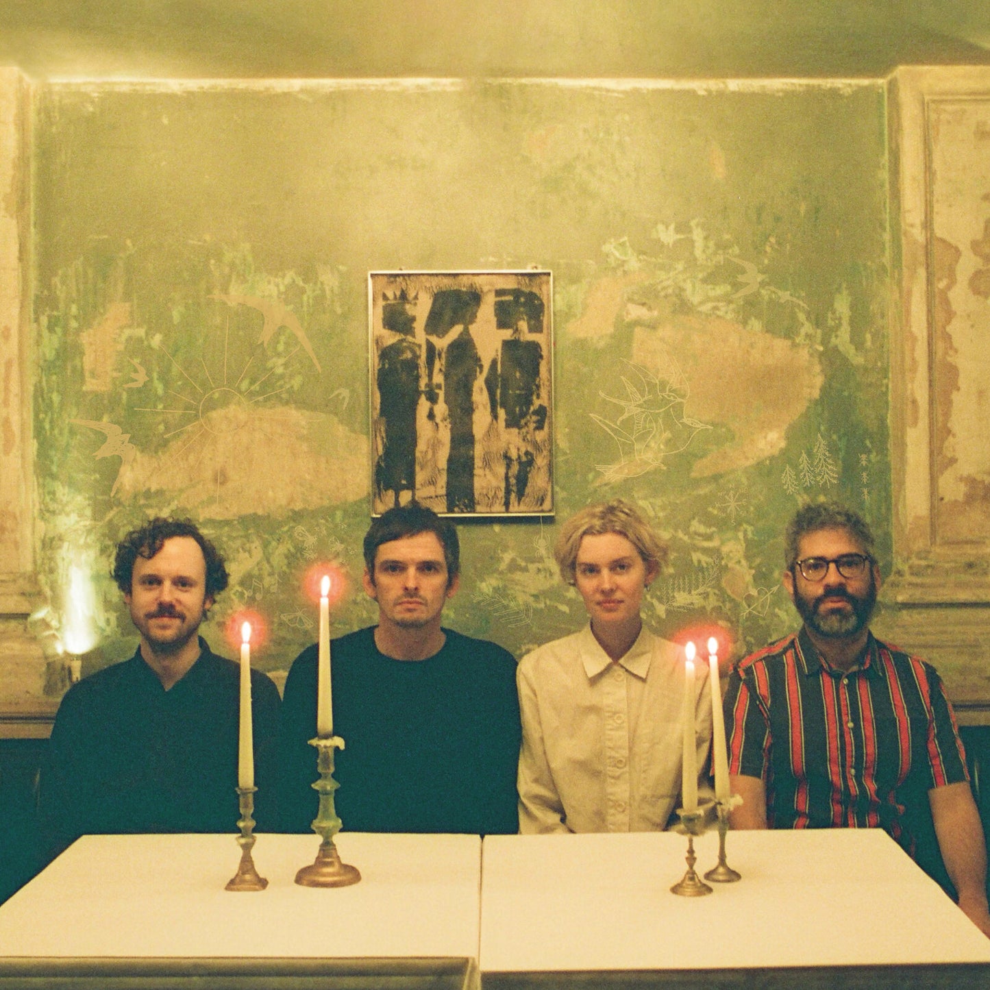Four people sit at a table with lit candles, against a painted wall.