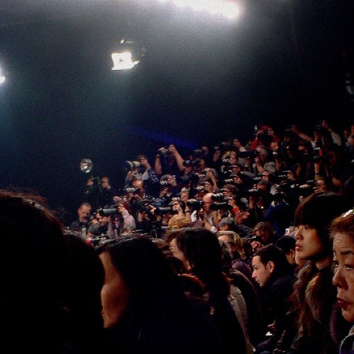 Crowd of people with raised cameras facing a stage or event.