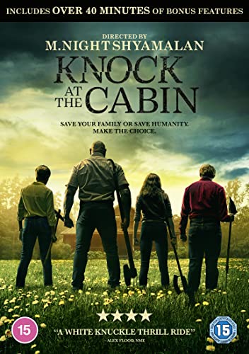 Four people stand in a field holding tools, facing a cabin at sunset.
