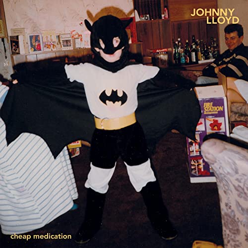 Child in a Batman costume stands in a room with adult figures.