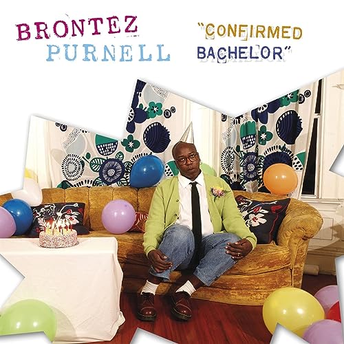 Brontez Purnell sits on a couch with balloons and a small cake.