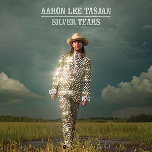 Aaron Lee Tasjan in a silver suit standing in a field.