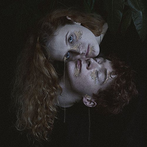 Two people with gold leaf on their faces lie close together.