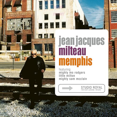 Man in black coat standing on train tracks beside album cover with cityscape background.
