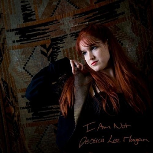Red-haired woman in dark clothing against a patterned wall.