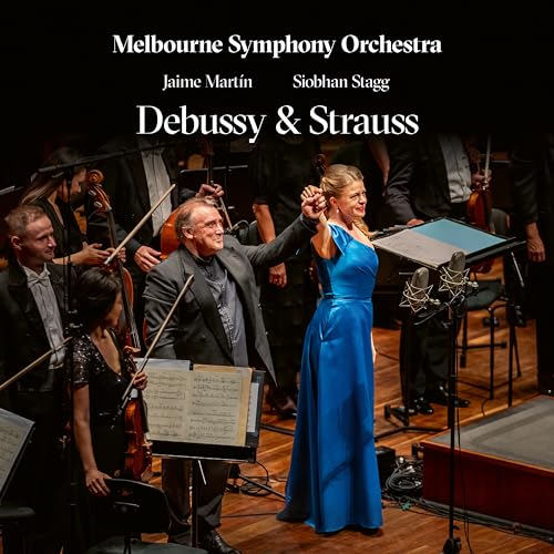 Orchestra performing with a soprano soloist on stage, concert hall setting.
