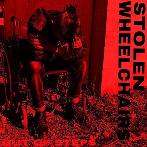 Person with spiked hair sits slumped in a wheelchair, red background.