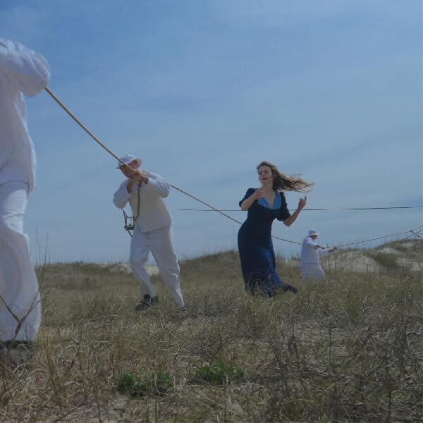 People in white and a woman in blue run across grassy dunes.