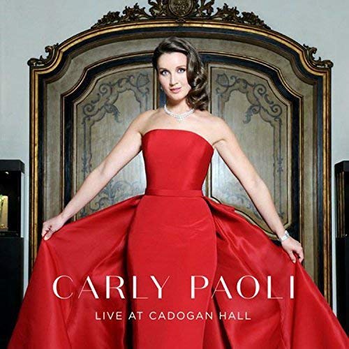 Carly Paoli in a red gown, standing before an ornate gold frame.