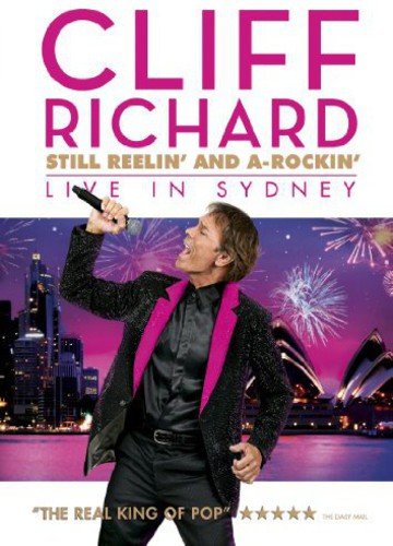 Cliff Richard singing with a microphone, Sydney Opera House and fireworks backdrop.