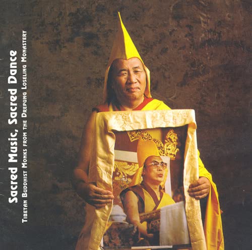 Buddhist monk in yellow hat and robes, holding a framed portrait.