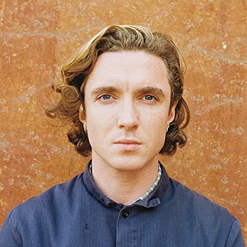 Close-up portrait of Keenan David with wavy hair against an orange background.