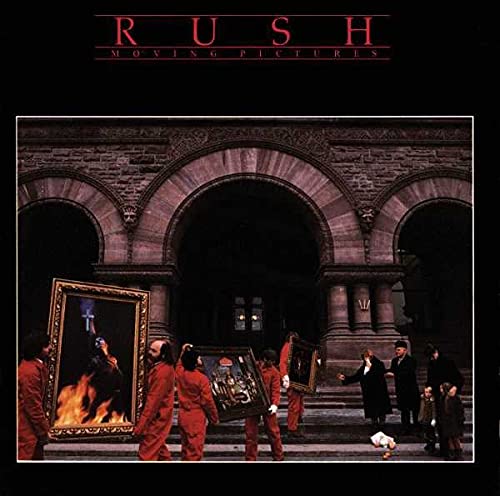 People in red jumpsuits carry framed paintings in front of a stone building.