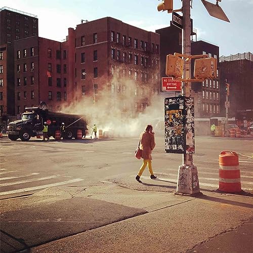City street scene with steam rising, a pedestrian, and brick buildings.